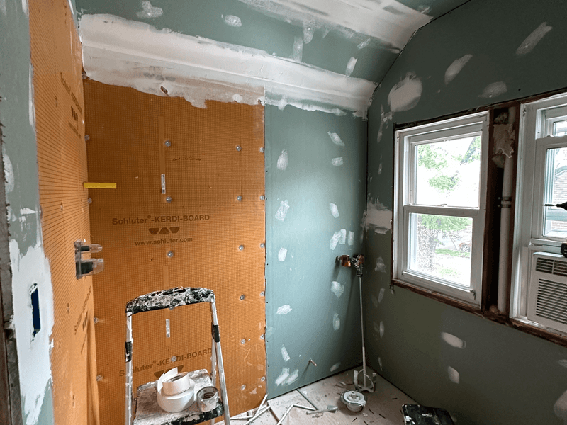 Bathroom renovation in progress in Bridgewater, New Jersey showing drywall and cement board installation with exposed studs, construction ladder, and natural light from window during a full bathroom remodel gut renovation