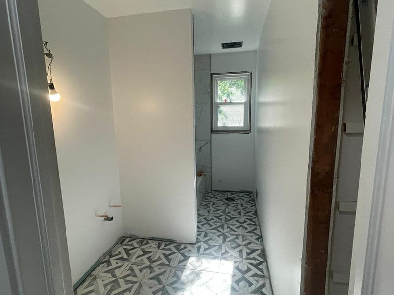 Bathroom remodel in progress in Hillsborough, New Jersey featuring newly installed geometric patterned gray and white floor tile, freshly painted white walls, and marble-look shower tile with natural light from window