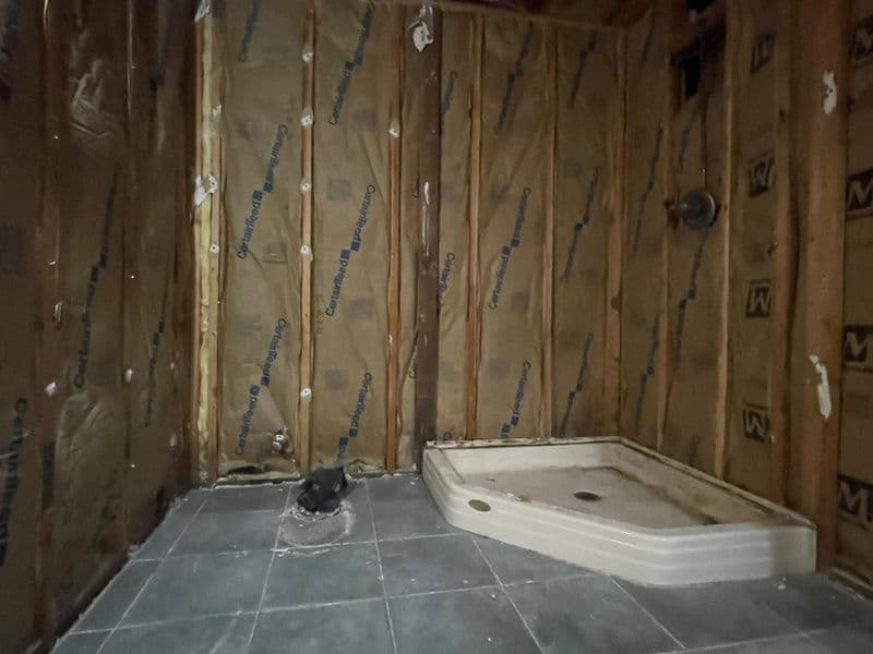 Bathroom remodel construction phase in Franklin Township, New Jersey showing kraft-faced insulation installed in walls, new shower base positioned, and gray slate tile flooring partially laid