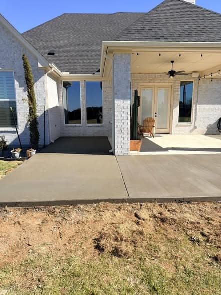 Freshly poured concrete patio extending from the back of a brick home with a covered porch area, smooth-finished concrete work by a New Jersey contractor serving Franklin Township