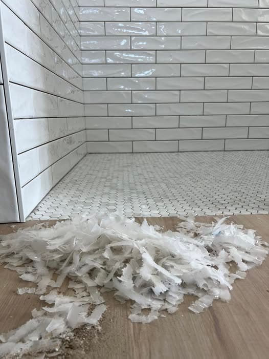 Drywall spackle debris and joint compound shavings cleaned up on a bathroom floor next to a freshly tiled shower with white subway tile walls and mosaic floor tile, drywall repair project in Watchung, New Jersey