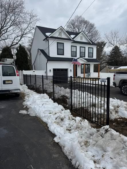 Black aluminum ornamental fence with gate installed in front of a white two-story home with snow on the ground, fencing installation services in Edison, New Jersey