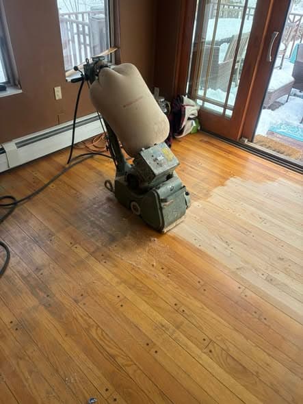 Drum floor sander refinishing natural pine hardwood floors in a living room with French doors, mid-process sanding stage showing bare wood alongside finished sections in Bernardsville, New Jersey