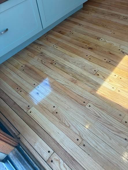 Glossy refinished natural oak hardwood floors with pegged plank details next to light blue kitchen cabinets, completed flooring installation in Bedminster, New Jersey