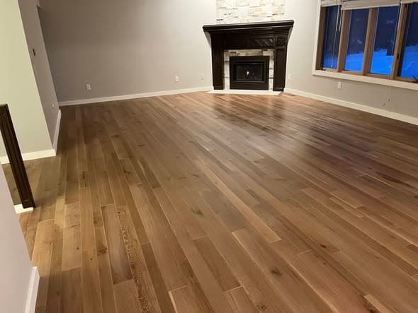 Wide-plank white oak hardwood floors with natural warm brown tones installed in a spacious living room with stone fireplace and gray walls in Bridgewater, New Jersey