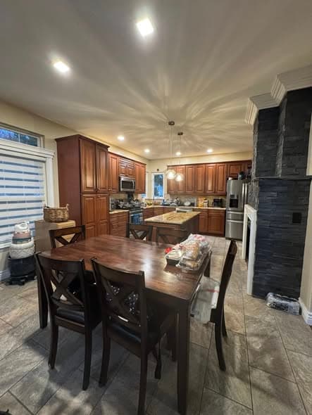 Finished kitchen and dining area renovation by a general contractor featuring warm cherry wood cabinets, granite countertops, stone accent column, stainless steel appliances, tile flooring, and eat-in dining space in a New Jersey home remodeling
