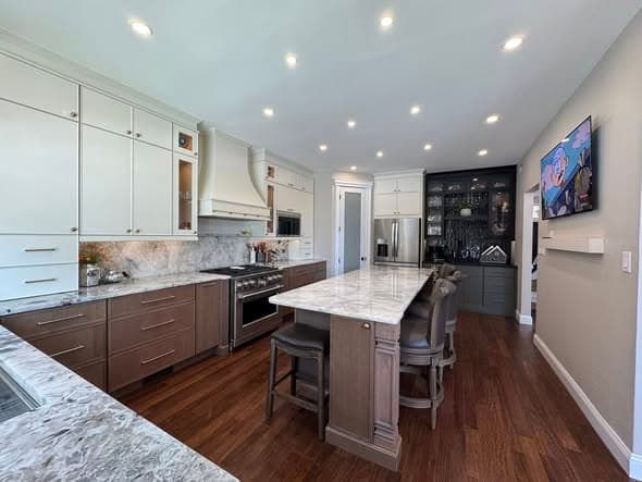 Bright open-concept kitchen renovation by a general contractor in the Bridgewater New Jersey area featuring two-tone white and brown cabinetry, marble countertops, large center island with seating, marble backsplash, stainless steel appliances, and dark hardwood flooring