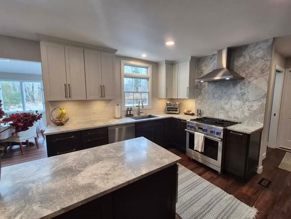 Modern kitchen renovation with two-tone gray and dark cabinetry, marble countertops, professional gas range, stainless steel hood, farmhouse sink, and hardwood floors completed by a general contractor serving Bridgewater and Hillsborough New Jersey
