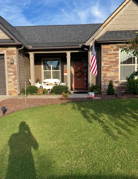 Exterior view of a single-story home with freshly painted warm tan siding, stone facade accents around the entryway, and an American flag by the front door, painting services in Bernardsville, New Jersey