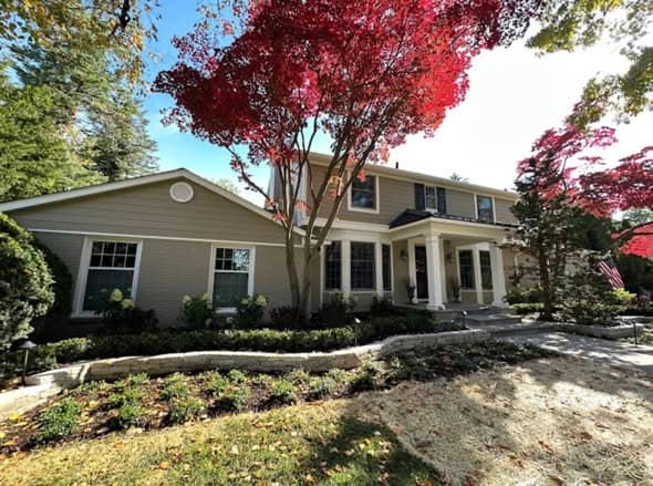 Two-story Colonial home with freshly painted light gray-green exterior, white trim, and dark green front door surrounded by mature landscaping, exterior painting services in Bridgewater, New Jersey