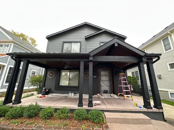 Exterior painting in progress on a two-story home being painted dark charcoal gray with black porch columns and trim, ladder and paint supplies on the front porch in Somerville, New Jersey