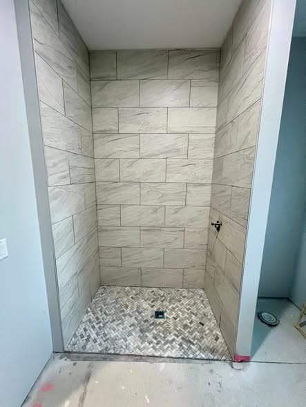 Custom walk-in shower tile installation with large-format gray marble-look wall tiles in a staggered brick pattern and herringbone mosaic marble floor tile with center drain, bathroom remodel in Hillsborough, New Jersey
