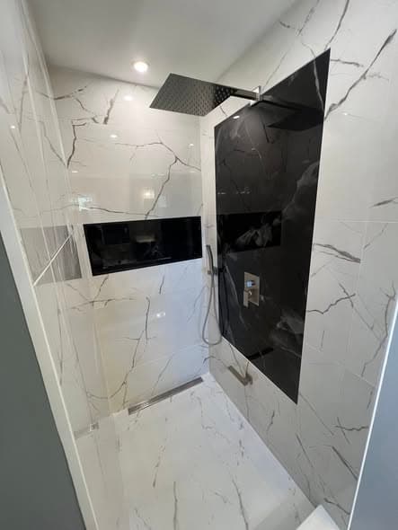 Luxury walk-in shower with dramatic black and white marble-look porcelain tile installation, large-format Calacatta-style wall tiles, black accent wall, recessed wall niche, and rain showerhead, modern bathroom remodel in Bridgewater, New Jersey