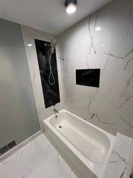 Modern bathtub surround tile installation with white Calacatta marble-look porcelain wall tiles and contrasting black accent panel with recessed niche for shower storage, white porcelain floor tile, bathroom remodel in Bound Brook, New Jersey